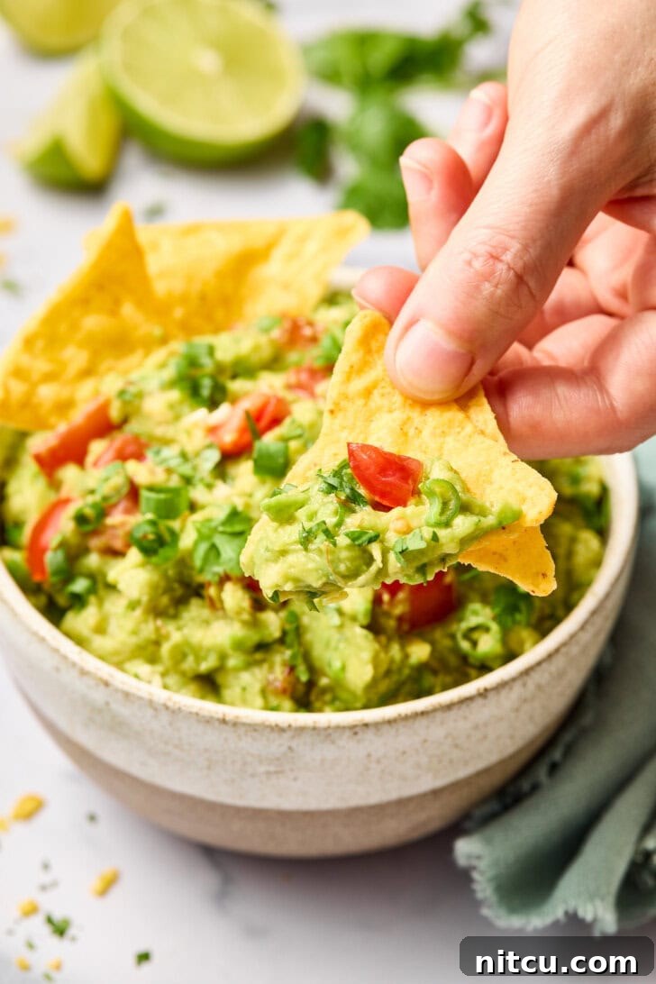Heavenly Guacamole Perfection 11 A hand scooping up a generous portion of creamy guacamole with a crispy tortilla chip.