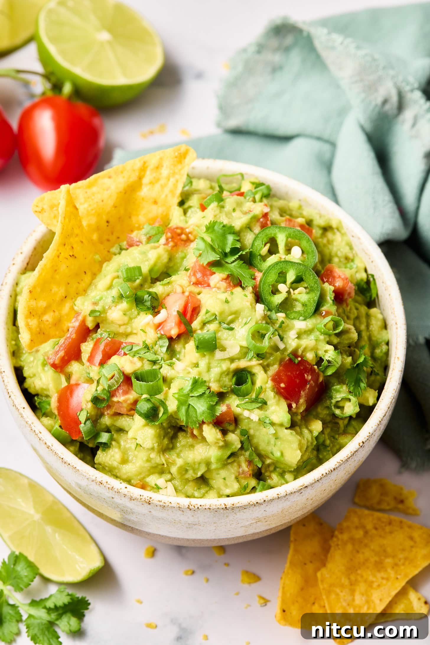 Holy-Guacamole A bowl of guacamole garnished with a lime wedge, cilantro, and tomato, served with a side of tortilla chips.