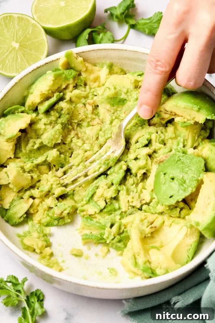 Heavenly Guacamole Perfection 7 A fork mashing ripe avocado in a bowl to achieve the desired creamy consistency.