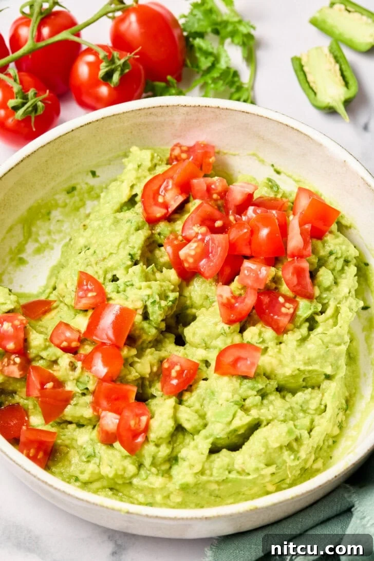 Heavenly Guacamole Perfection 9 Diced tomatoes being gently mixed into the avocado mixture, adding color and texture.