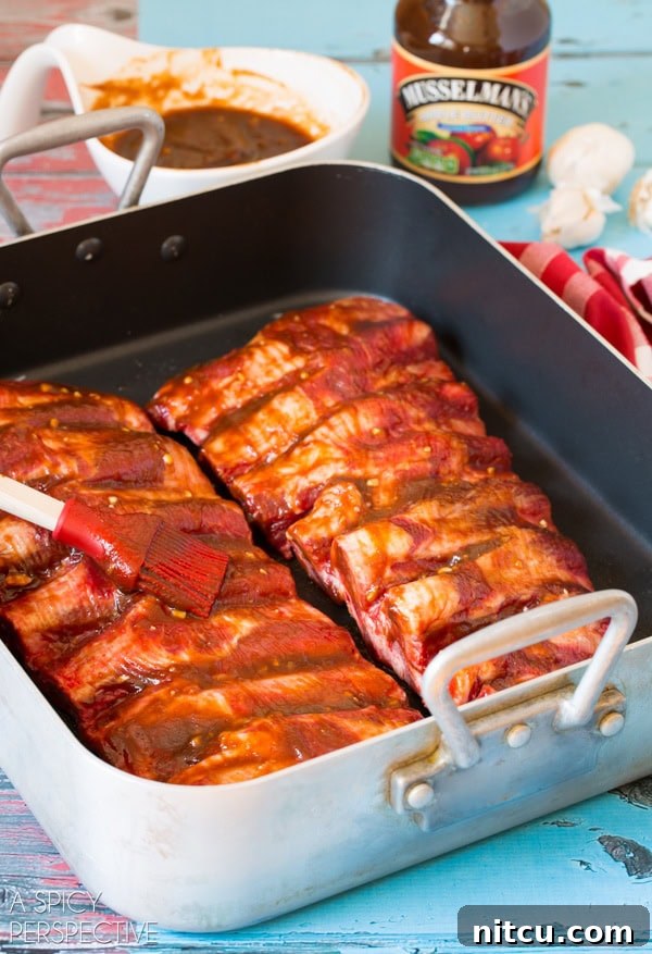Sticky Soy-Glazed Asian Short Ribs 5 Beef ribs covered in cooking sauce sitting in baking pan with brush.