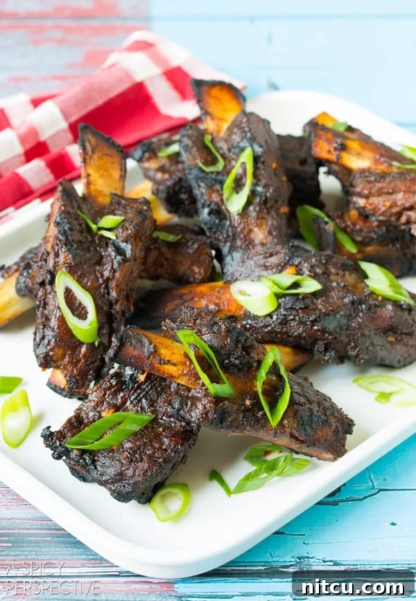 Sticky Soy-Glazed Asian Short Ribs 6 Closeup of cooked Asian beef ribs on white serving plate topped with slivers of fresh scallions.