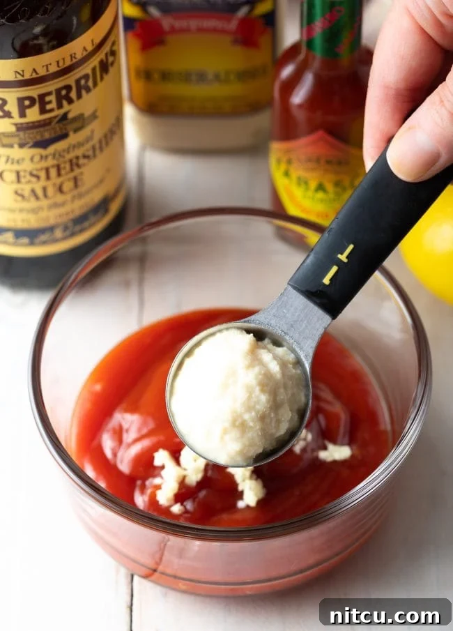 Horseradish being carefully added to a small bowl containing ketchup, the first step in creating homemade cocktail sauce.