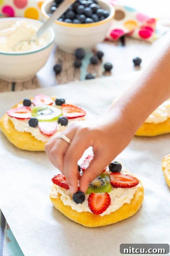 Sweet Start Fruit Pizza 5 Easy Fruit Pizza for Breakfast being assembled, with fresh fruit being added to the cream cheese topping.