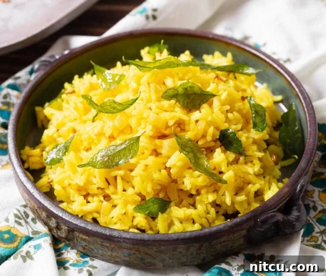A bowl of fragrant Indian rice, garnished with fresh curry leaves and a vibrant sprinkle of turmeric.