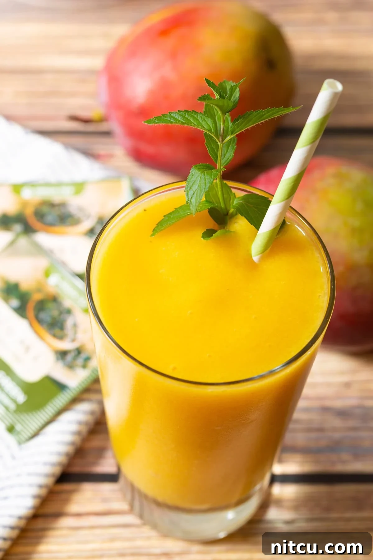 Vibrant Mango Green Tea Refresher 2 A vibrant mango green tea smoothie in a glass, garnished with fresh mint and a stylish straw. The texture is creamy and inviting, promising a refreshing and healthy start to the day.