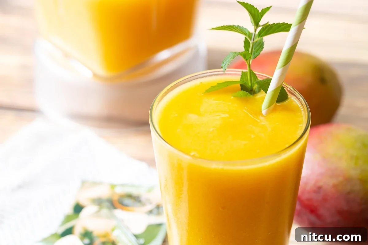 Vibrant Mango Green Tea Refresher 4 A beautifully presented Mango Green Tea Smoothie in a clear glass, garnished with fresh mint and a striped straw, invitingly ready to be enjoyed.