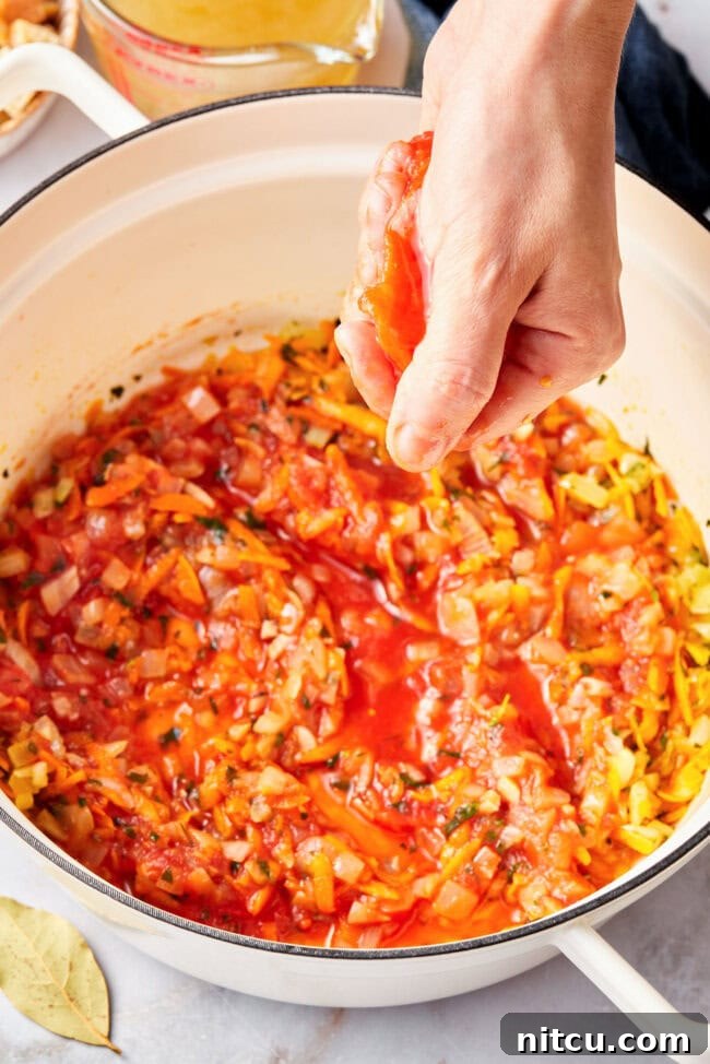 Rustic Italian Tomato Bread Soup Pappa al Pomodoro 7 A hand squishing a whole peeled San Marzano tomato over a pot, breaking it into irregular pieces for the soup.