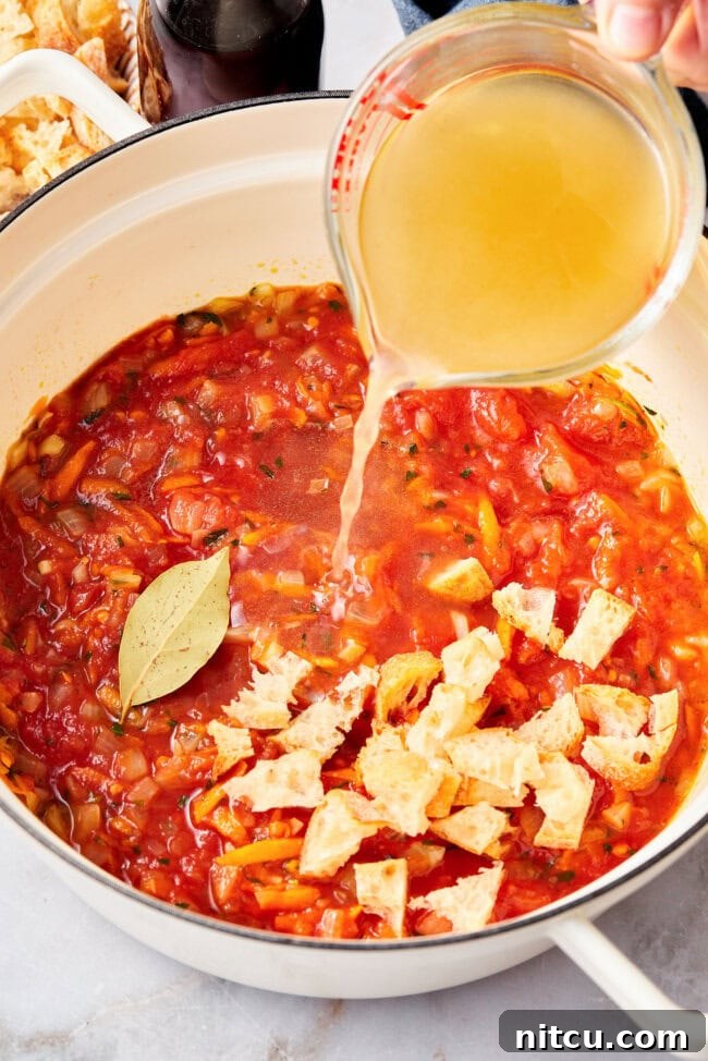 Rustic Italian Tomato Bread Soup Pappa al Pomodoro 8 Vegetable broth being poured into a large stockpot filled with tomatoes, vegetables, and bread, for making tomato soup.