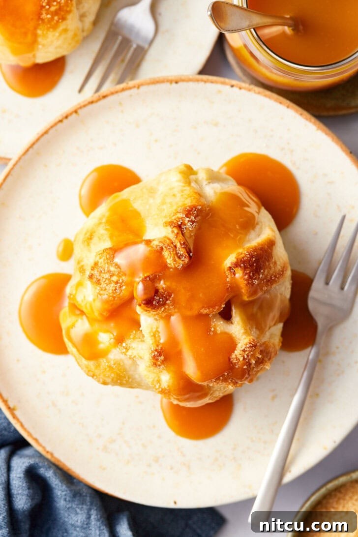Flaky Apple Pastry Pockets 4 Baked apple wrapped in puff pastry on a plate with caramel drizzled on top.