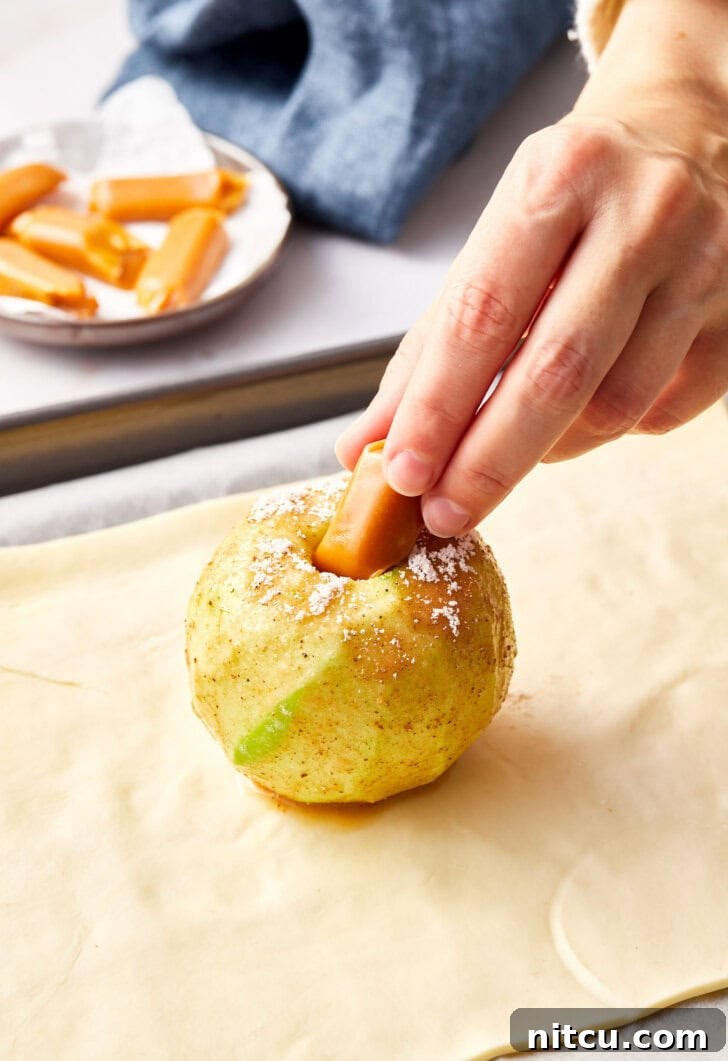 Flaky Apple Pastry Pockets 9 Peeled apple being stuffed with caramel candy for apple pie bombs.