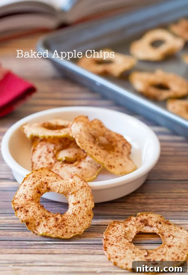 Golden Apple Crisps 2 Baked Apple Chips in a white bowl with two sitting in the front on the wood surface.