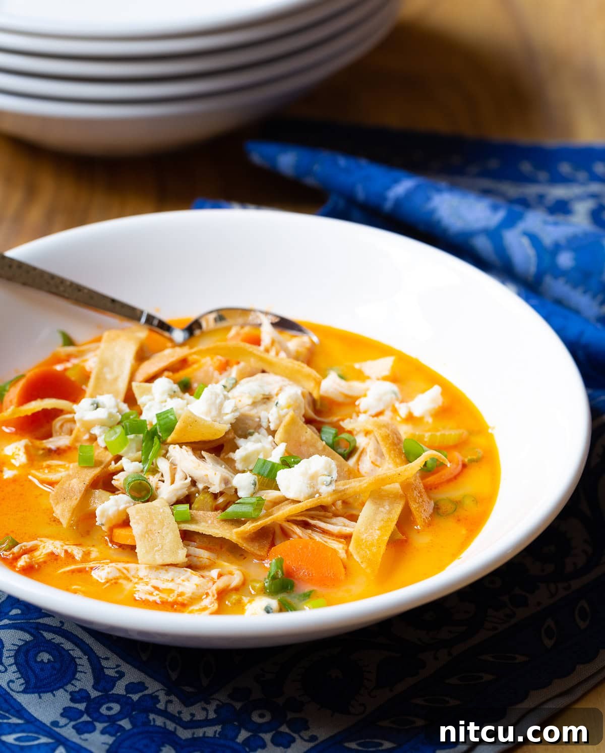 Buffalo-Chicken-Soup Close-up of a rustic white bowl filled with Easy Buffalo Chicken Soup, topped generously with golden crispy tortilla strips and finely chopped green onions, ready to be enjoyed.