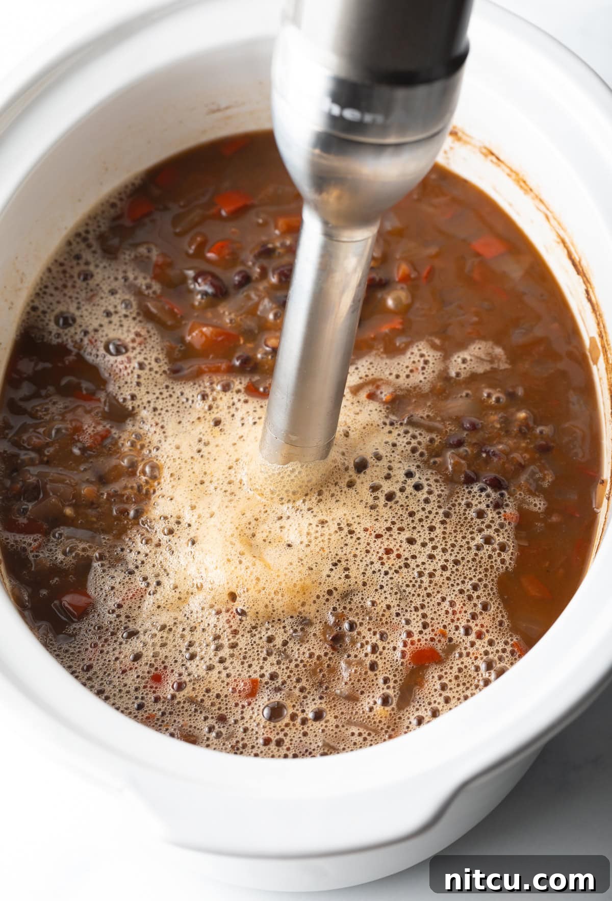 Slow Cooker Black Bean Bliss 6 Immersion blender mixing black bean soup in a slow cooker, creating a creamy texture.