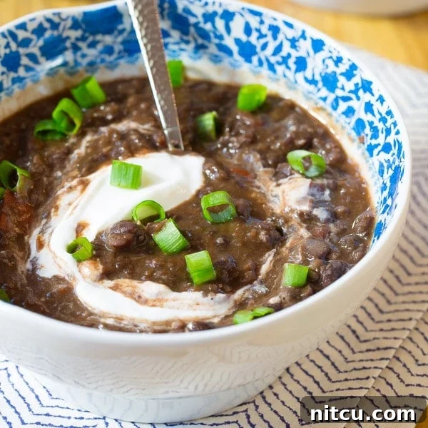 Slow Cooker Black Bean Bliss 7 Closeup of a bowl of black bean soup topped with sour cream and chopped scallions, highlighting the fresh garnishes.