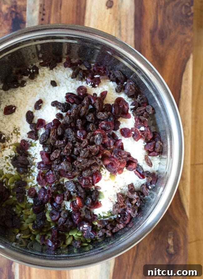 Dried fruit added to nuts and oat mixture in a mixing bowl.