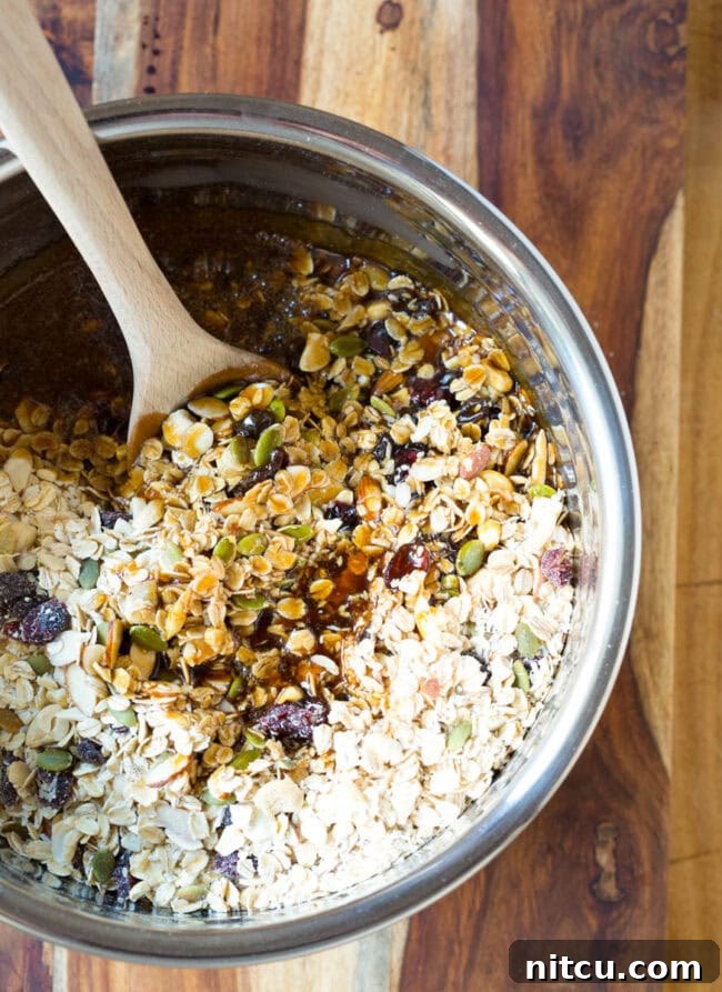Granola mixture with honey in a mixing bowl with a wooden spoon.