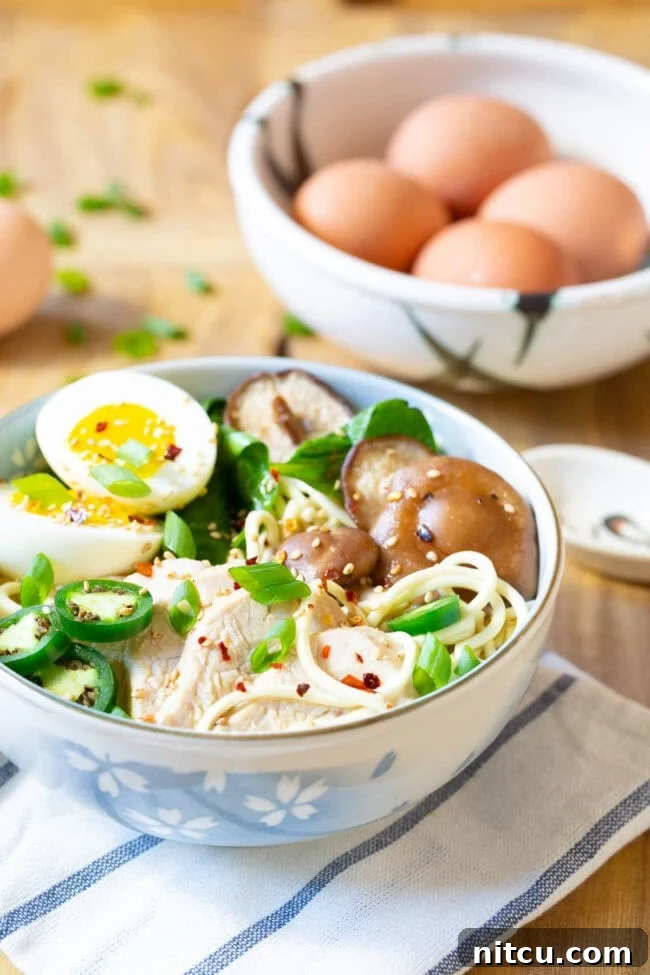 A steaming bowl of Slow Cooker Chicken Ramen Noodle Soup, garnished with a soft-boiled egg, fresh spinach, and scallions, showcasing its rich broth and vibrant ingredients.