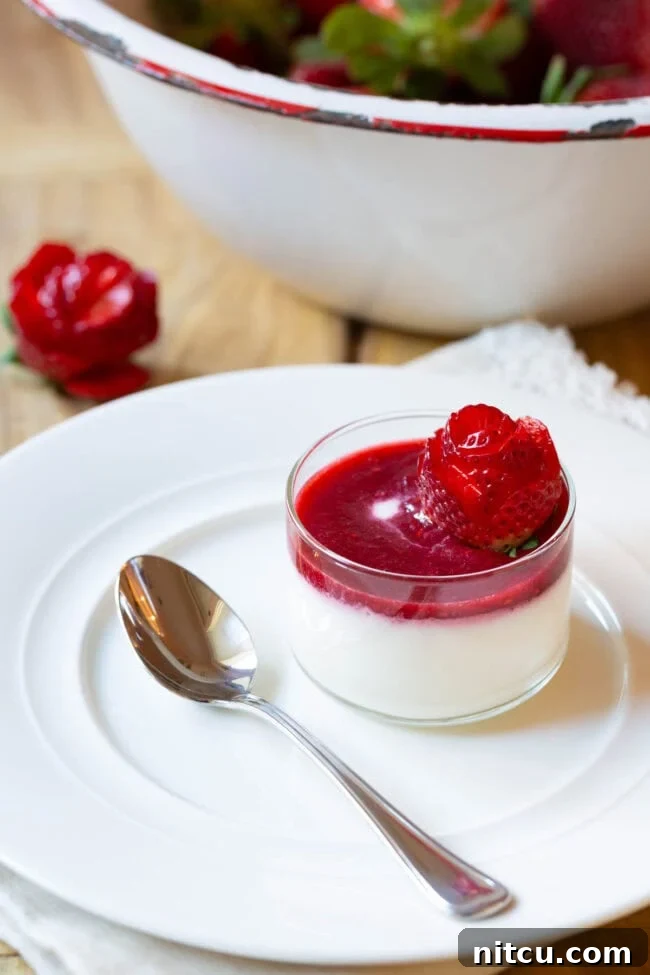 Small glass dish with silky Swedish Cream adorned with vibrant berry compote and an elegant strawberry rose, ready to be enjoyed.