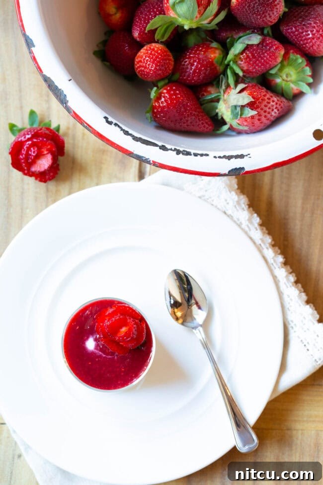 Top down view of a small glass dish showcasing silky Swedish Kreme generously topped with a rich berry compote and a beautiful strawberry rose.