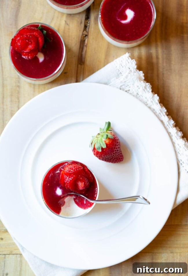 Top down view of a glass dish containing silky Swedish Cream, berry compote, and a strawberry rose. A whole, fresh strawberry is placed beside the dish.