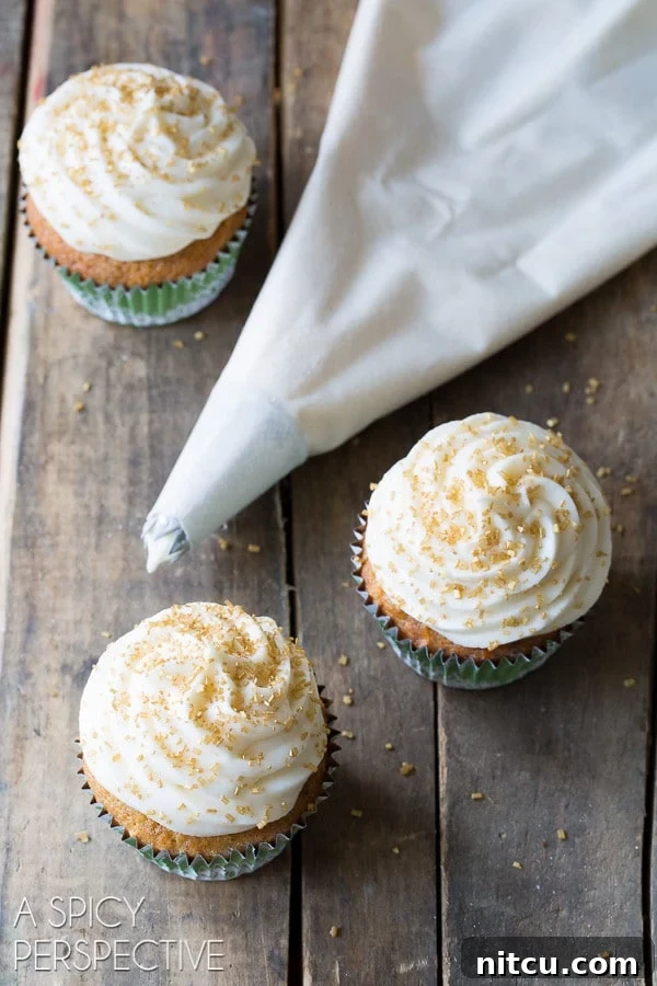 Delicious Hummingbird Cake Cupcakes with Sour Cream Frosting, perfect for spring gatherings. A piping bag filled with creamy frosting next to a selection of freshly decorated hummingbird cupcakes.