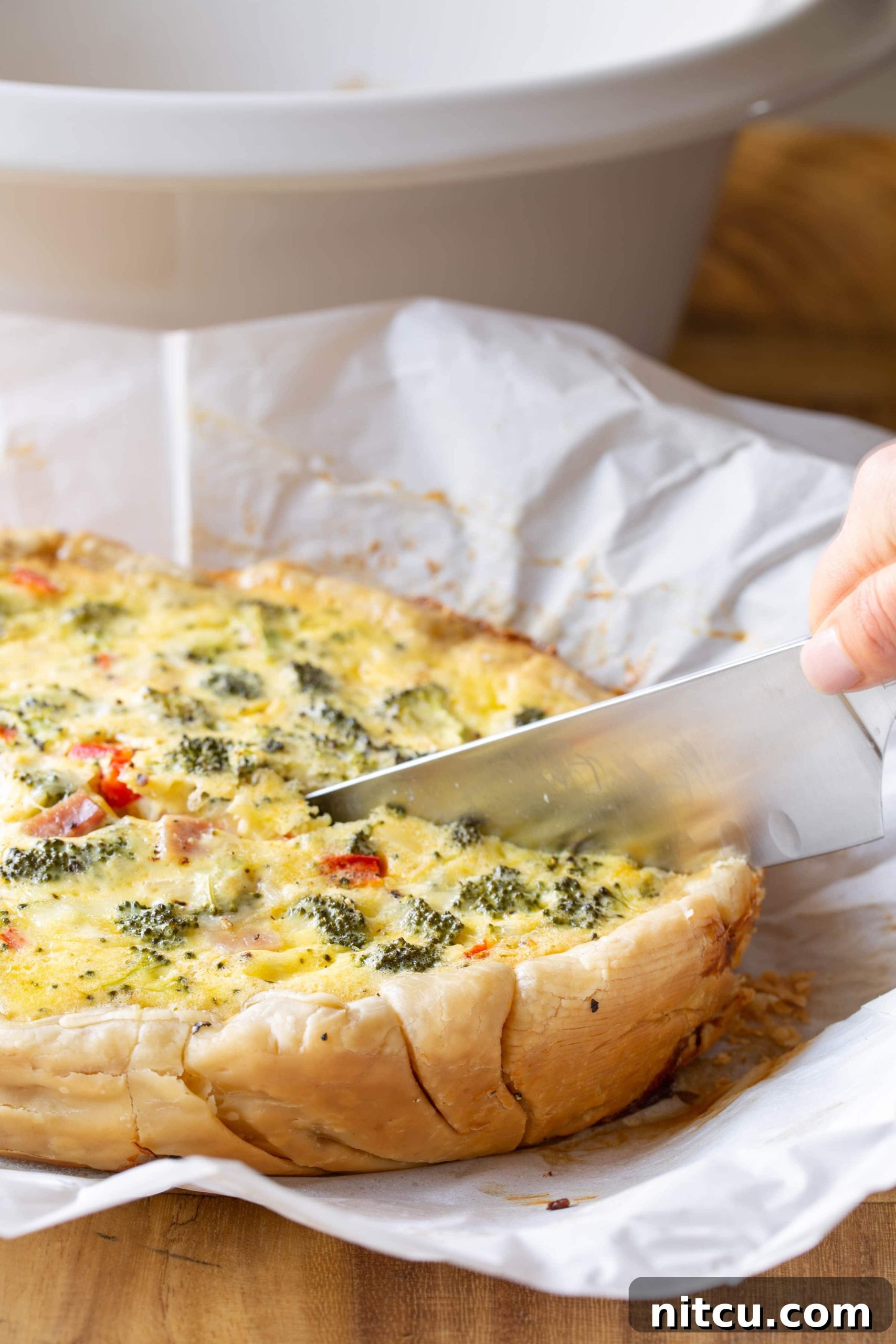 A sharp knife cutting breakfast quiche that's on a piece of parchment paper.