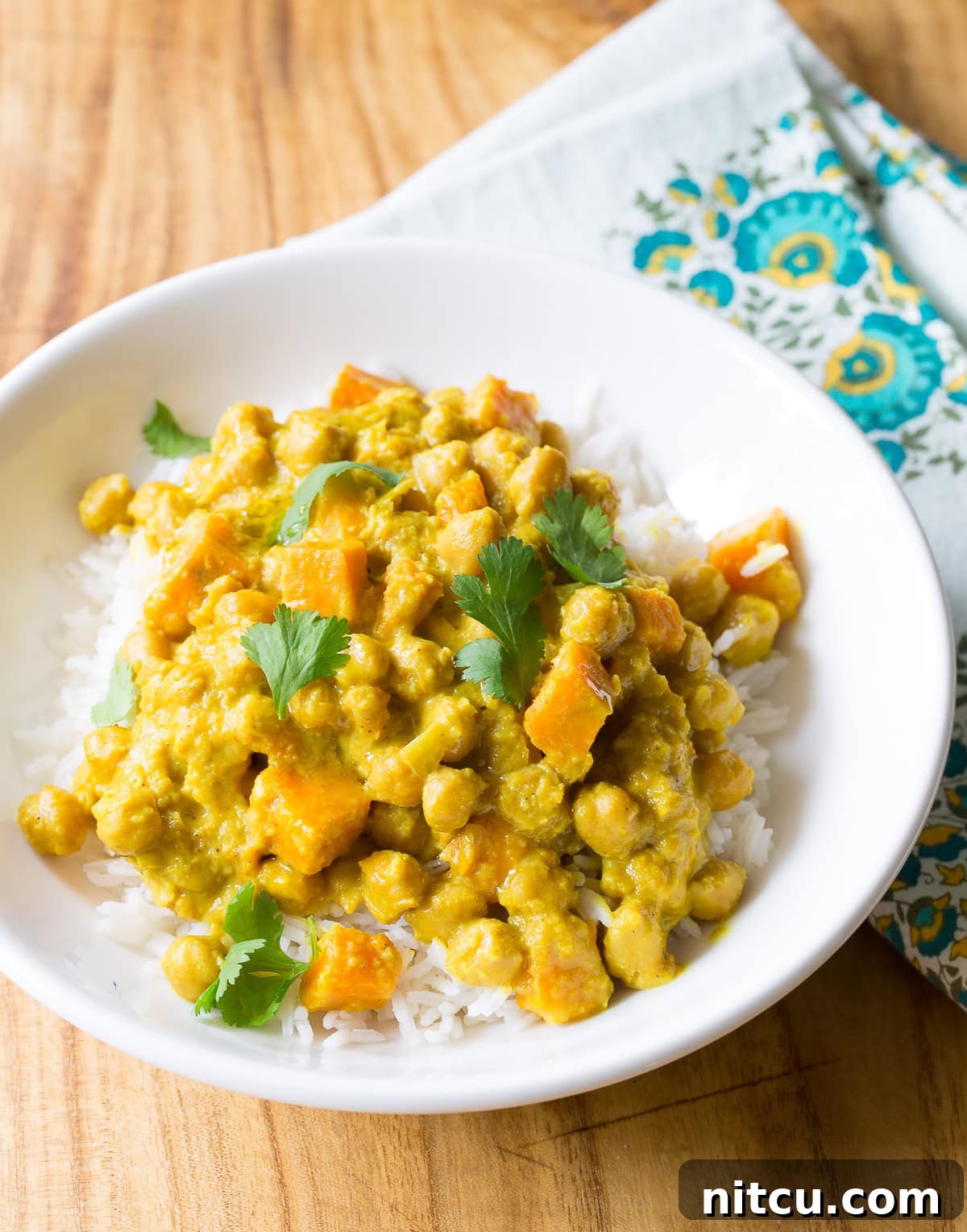 A white plate with a serving of crockpot chickpea curry on a bed of white rice, garnished with fresh cilantro.