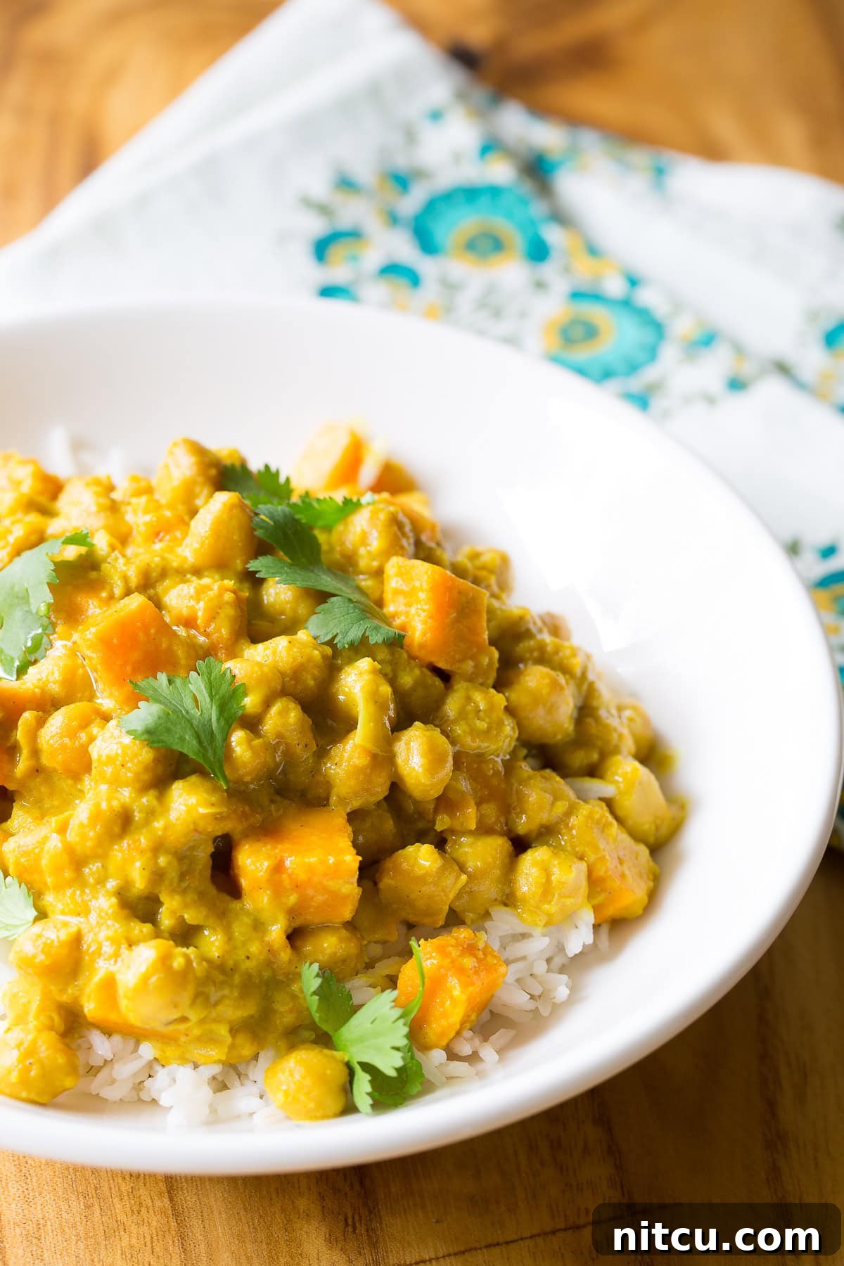 A close-up of a white plate featuring a portion of chickpea curry on white rice, ready to be enjoyed.