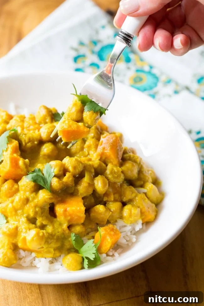 A fork holding a bite full of crockpot chickpea curry above a plate of curry, ready to be eaten.