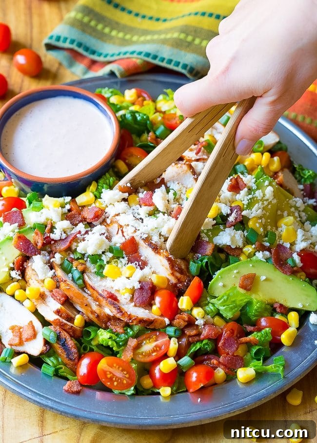 Fiesta Chicken Salad 7 Hand is tossing the Mexican chicken salad in a bowl with wooden tongs.