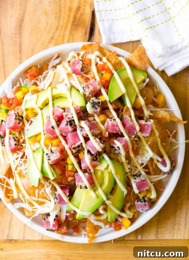 Aloha Ahi Poke Nachos 2 Ahi tuna nachos overhead view, white bowl loaded with crispy wonton chips, cubes of seared ahi tuna, mango pico de gallo, shredded cabbage, avocado slices, and a drizzle of wasabi mayo.