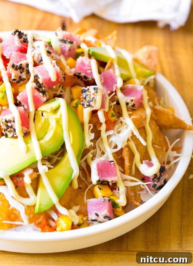 Aloha Ahi Poke Nachos 3 White bowl loaded with crispy wonton chips, cubes of seared ahi poke, mango pico de gallo, shredded cabbage, avocado slices, and a drizzle of wasabi mayo.