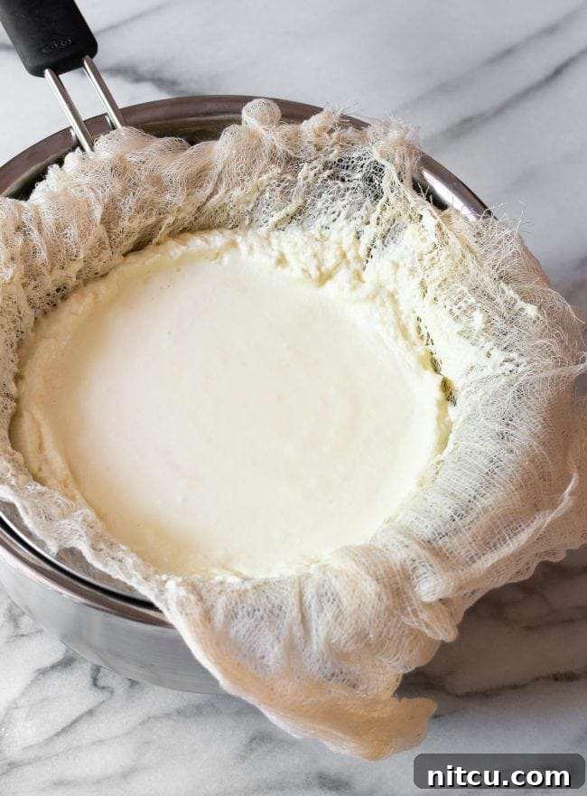 Crafting Creamy Ricotta at Home 10 A mound of solidified homemade ricotta cheese resting within the cheesecloth in a sieve, with the whey having drained into the bowl below, showcasing the finished product.