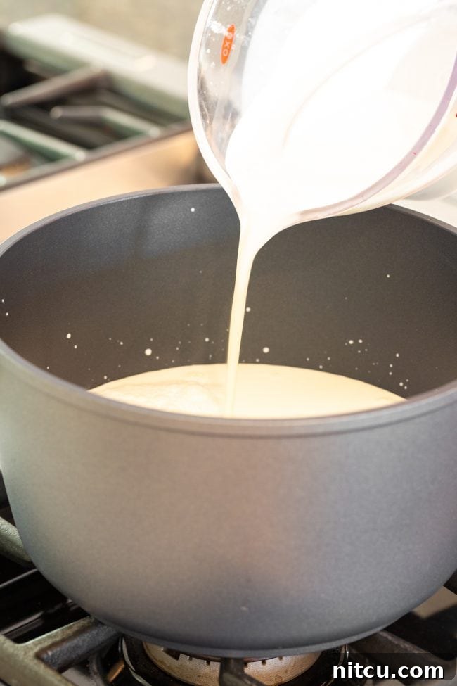 Crafting Creamy Ricotta at Home 5 Pouring fresh whole milk from a glass measuring cup into a large metal stock pot, ready for heating.
