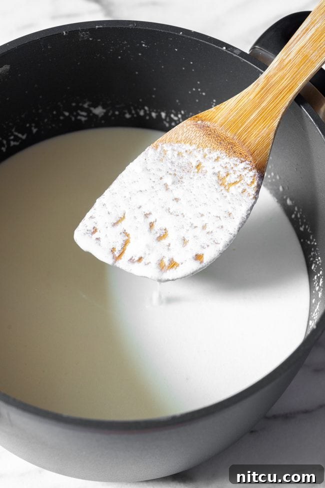 Crafting Creamy Ricotta at Home 7 A wooden spatula showing a thin coating of early curds over the cooking ricotta mixture in a large black pot, indicating the milk is beginning to curdle.