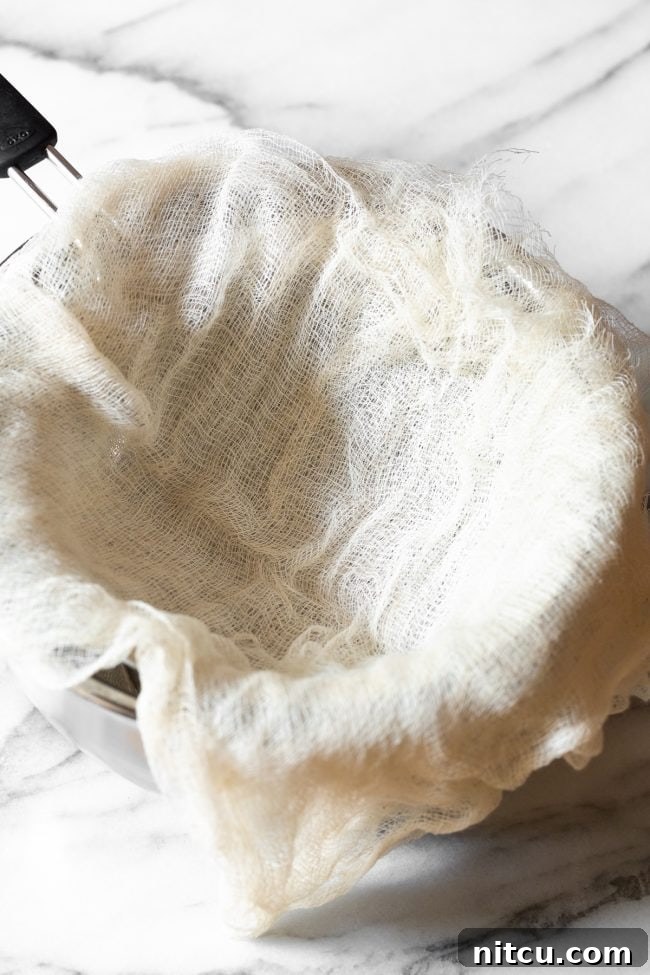 Crafting Creamy Ricotta at Home 8 A clean cheesecloth meticulously laid over a fine-mesh sieve, which is placed atop a metal bowl, preparing for the straining process.