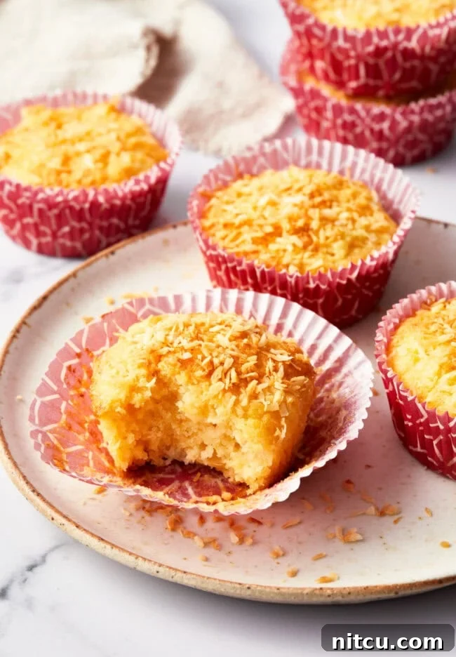 Tropical Sunrise Muffins 2 A tropical breakfast muffin with a bite taken out of it on a white plate. more muffins are in the background.