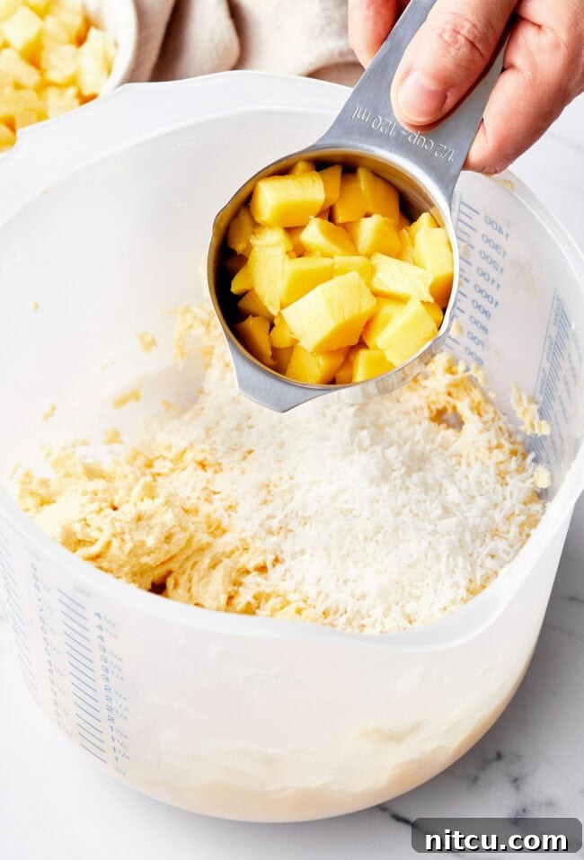Tropical Sunrise Muffins 6 A hand holding a cup of fresh mango above the bowl of muffin batter.