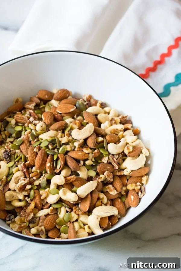 A large mixing bowl filled with a generous assortment of raw whole mixed nuts and bright green pepitas, ready for coating.