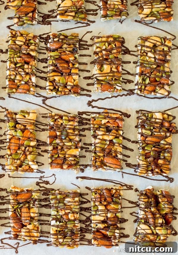 Top-down view of 16 perfectly cut nut bars generously drizzled with dark chocolate, neatly arranged on parchment paper.