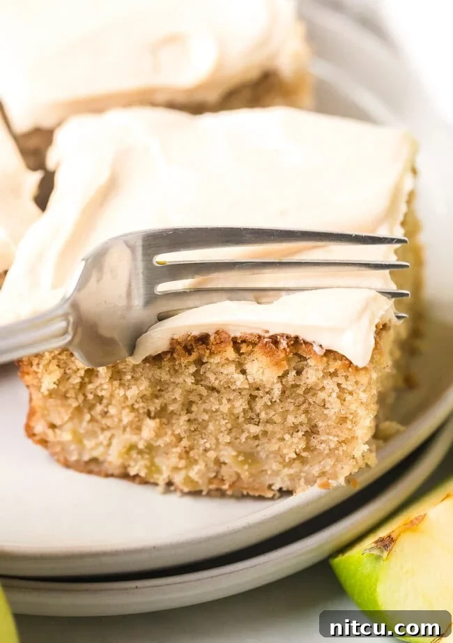A delectable slice of apple cake topped with generous salted caramel frosting, with a fork gently cutting into it, ready for a bite.