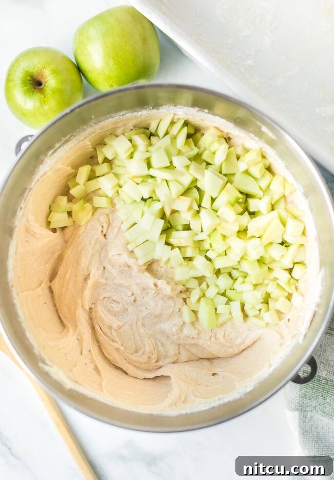 Cake batter with freshly chopped apples in a large mixing bowl, ready for baking.