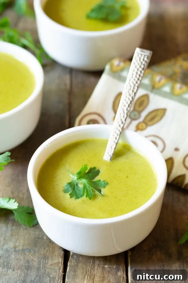 White small bowl of creamy poblano pepper soup garnished with a cilantro leaf.