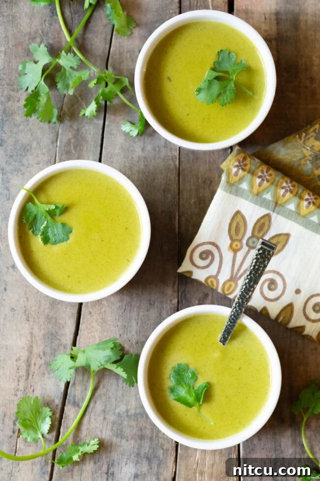 Top down view 3 white small bowls of creamy green soup, each garnished with a cilantro leaf.