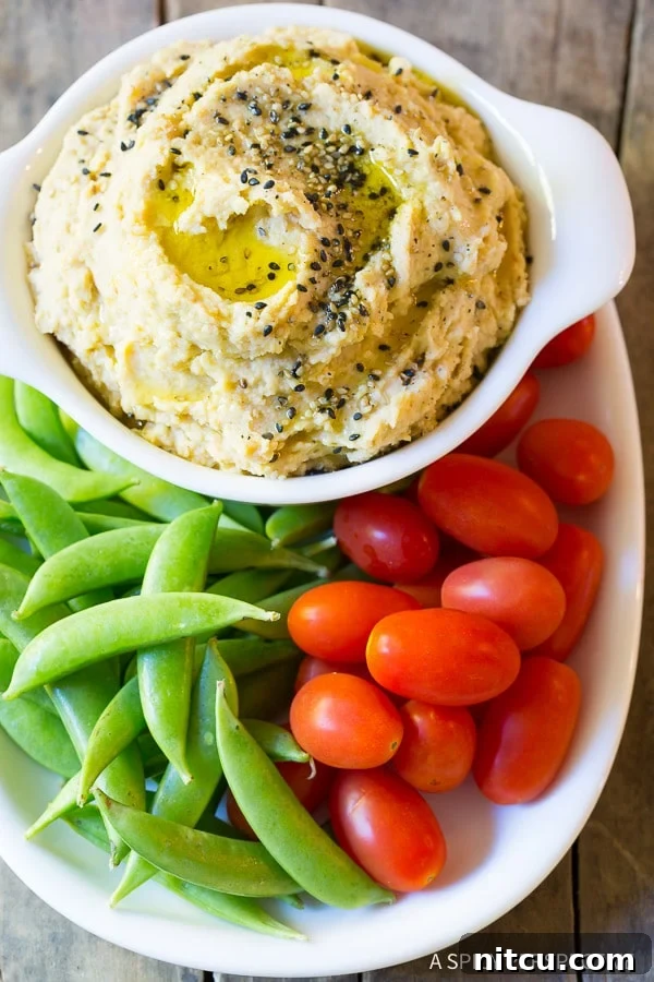 Umami Miso Hummus 2 Top down view plate of fresh sweet peas and grape tomatoes snuggled around a white dish of sesame miso hummus.