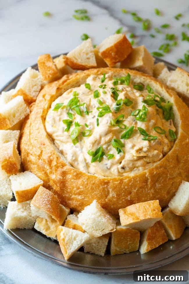 Velvety Sausage Cheese Dip 2 A beautiful sourdough bread bowl brimming with rich, creamy sausage cheese dip, garnished with fresh green onions and surrounded by golden bread cubes for dipping on a rustic wooden platter.