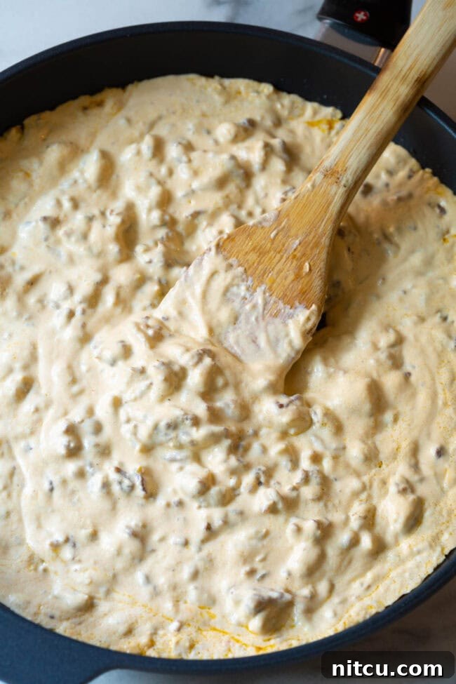 Velvety Sausage Cheese Dip 5 The rich, creamy sausage cheese dip simmering to perfection in a large skillet, with a wooden spoon ready to stir.