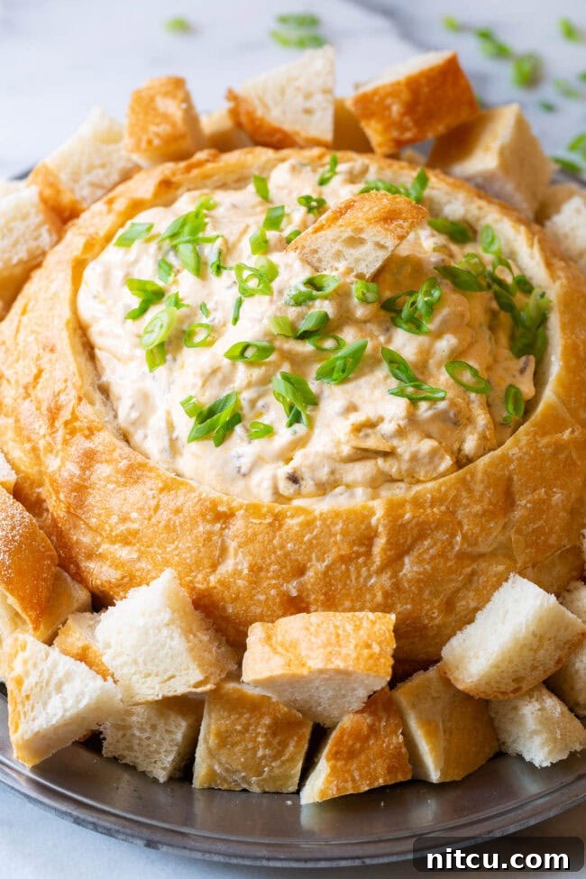 Velvety Sausage Cheese Dip 7 A bountiful sourdough bread bowl filled with creamy sausage cheese dip, surrounded by an array of dippable bread chunks, inviting guests to enjoy.