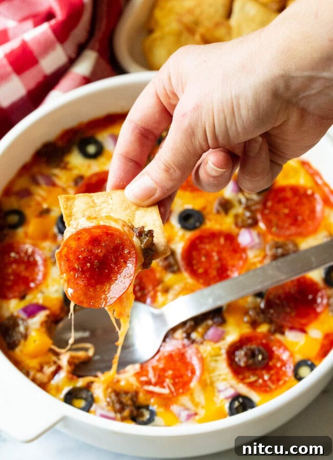 Fully Loaded Pizza Dip 9 Hand using a pita chip to scoop a bite of pepperoni pizza dip.